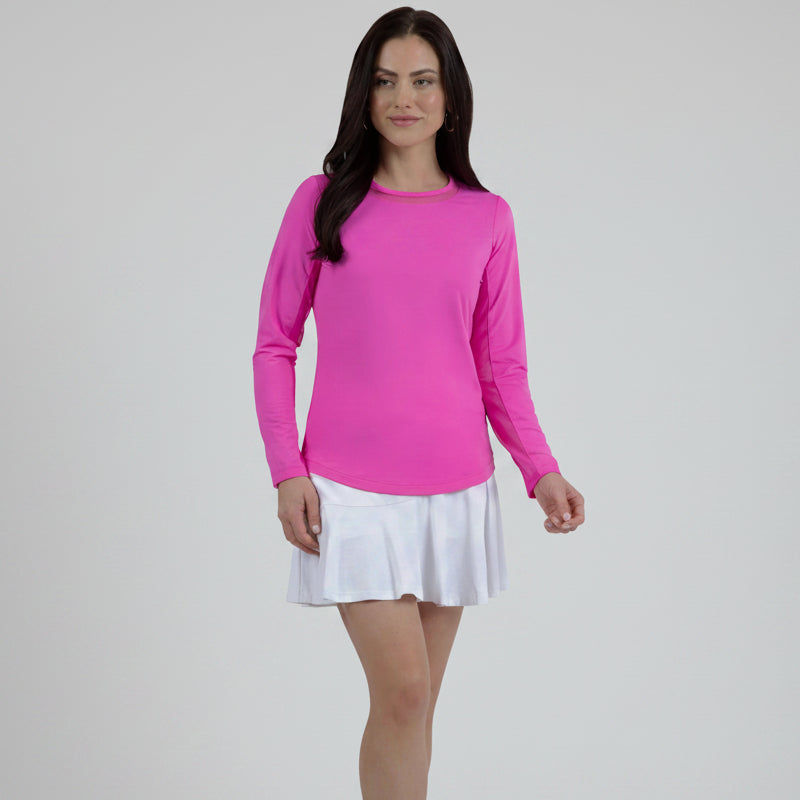 A woman wearing a long sleeve hot pink crew neck top with a mesh inlay around the neck and a flared tennis skirt.