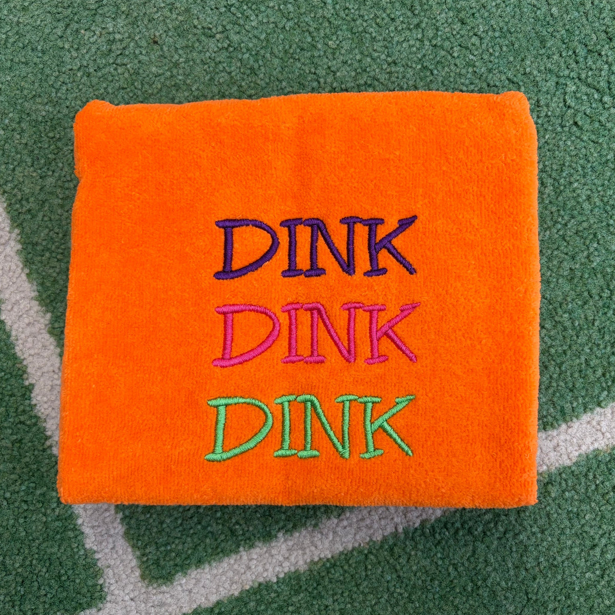Orange towel embroidered with three stacked DINK words in purple, pink, and green