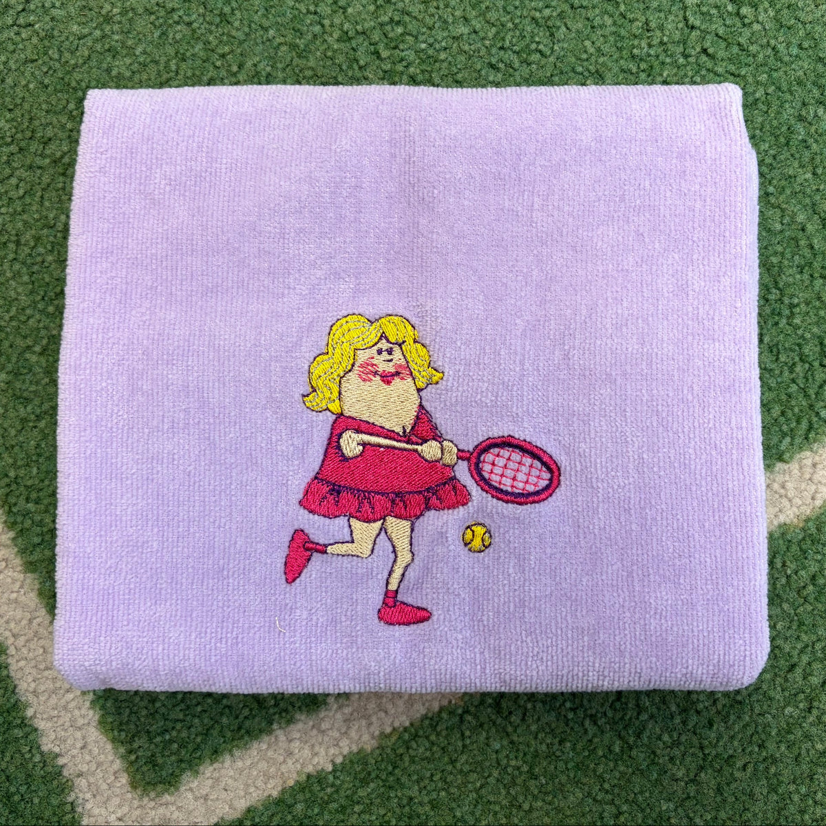 Lavender towel embroidered with a tennis-playing character holding a racket and ball