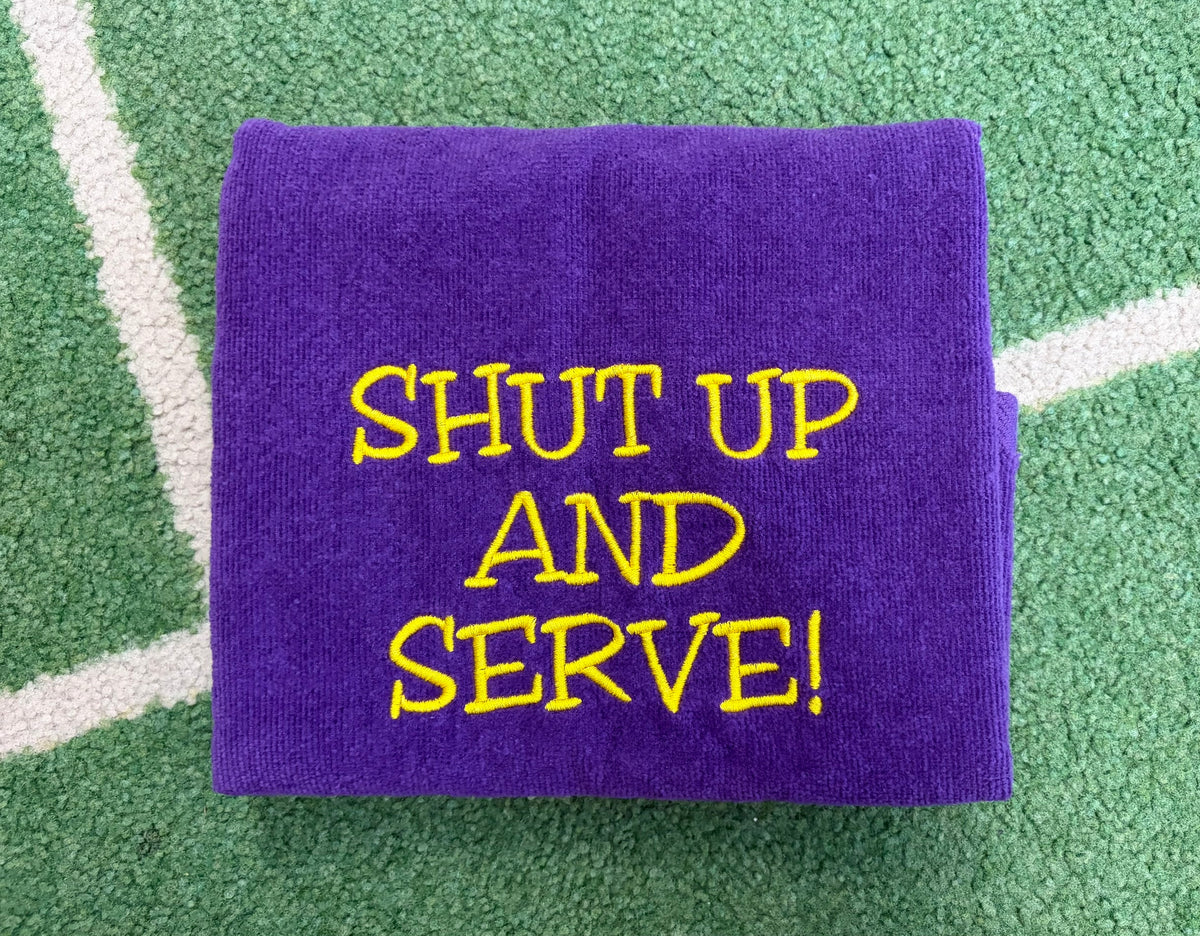 Purple towel embroidered with yellow SHUT UP AND SERVE lettering