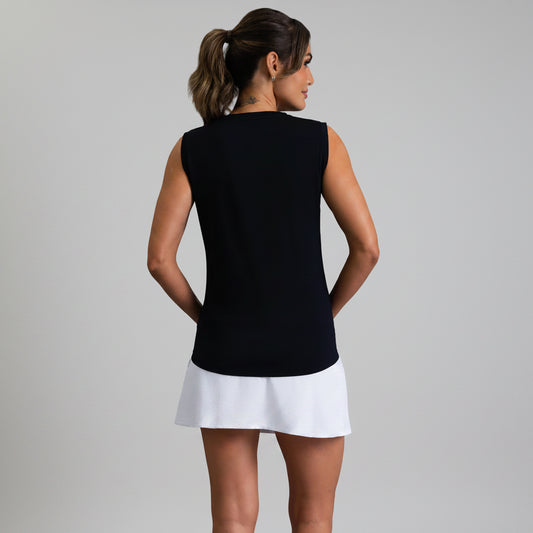 Back view of a woman wearing a black sleeveless muscle tank and white skirt on a gray background