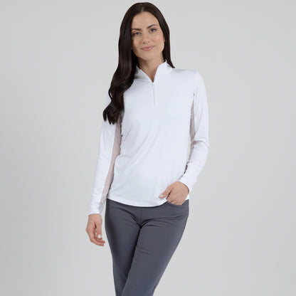 A woman wearing a long sleeve white mock neck top with a mesh underarm panel, paired with grey pants.