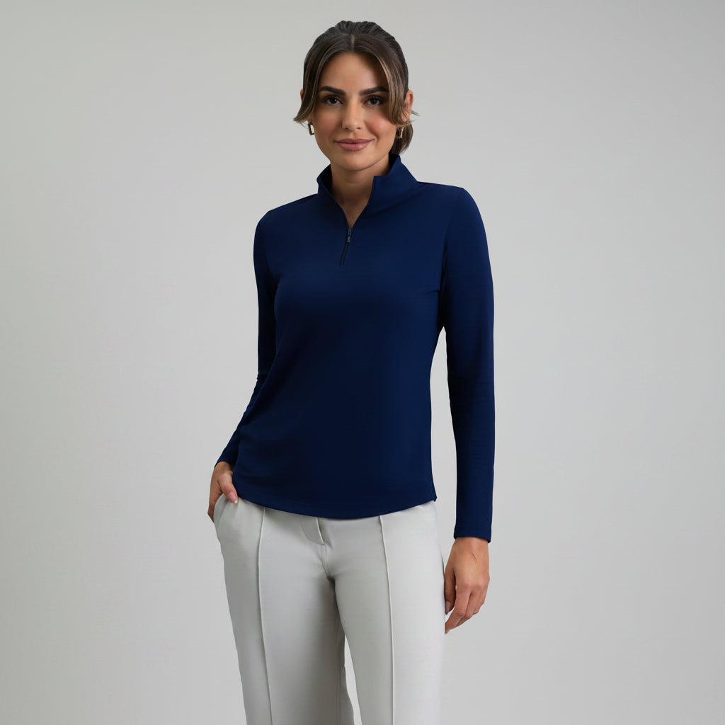 Woman wearing a classic navy long-sleeve mock zip top and light-colored pants on a gray background