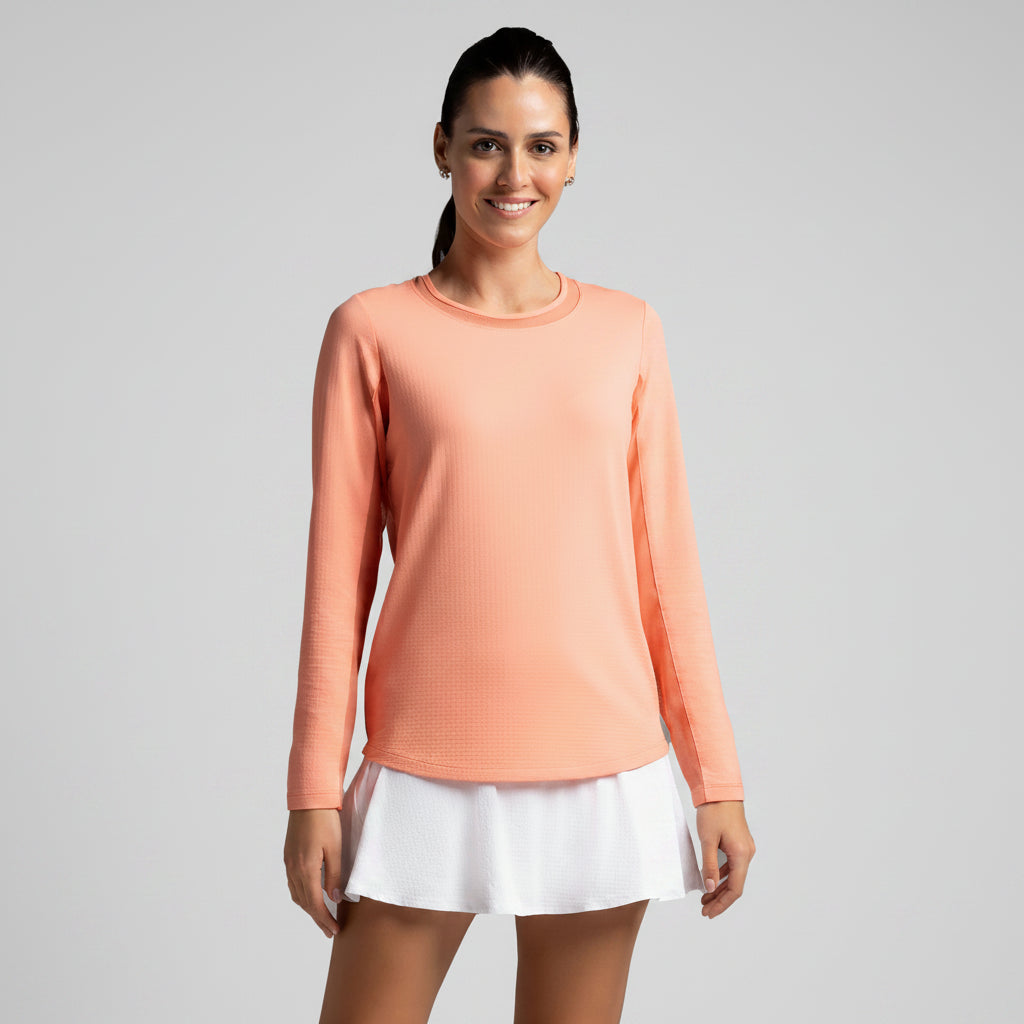 Woman wearing a peach long-sleeve top and white tennis skirt on a gray background