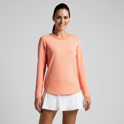 Woman wearing a peach long-sleeve top and white tennis skirt on a gray background