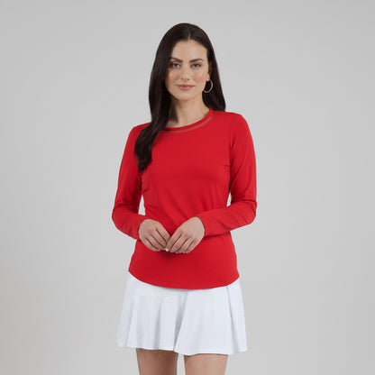 A woman wearing a long sleeve red crew neck top with a mesh inlay around the neck and a flared tennis skirt.