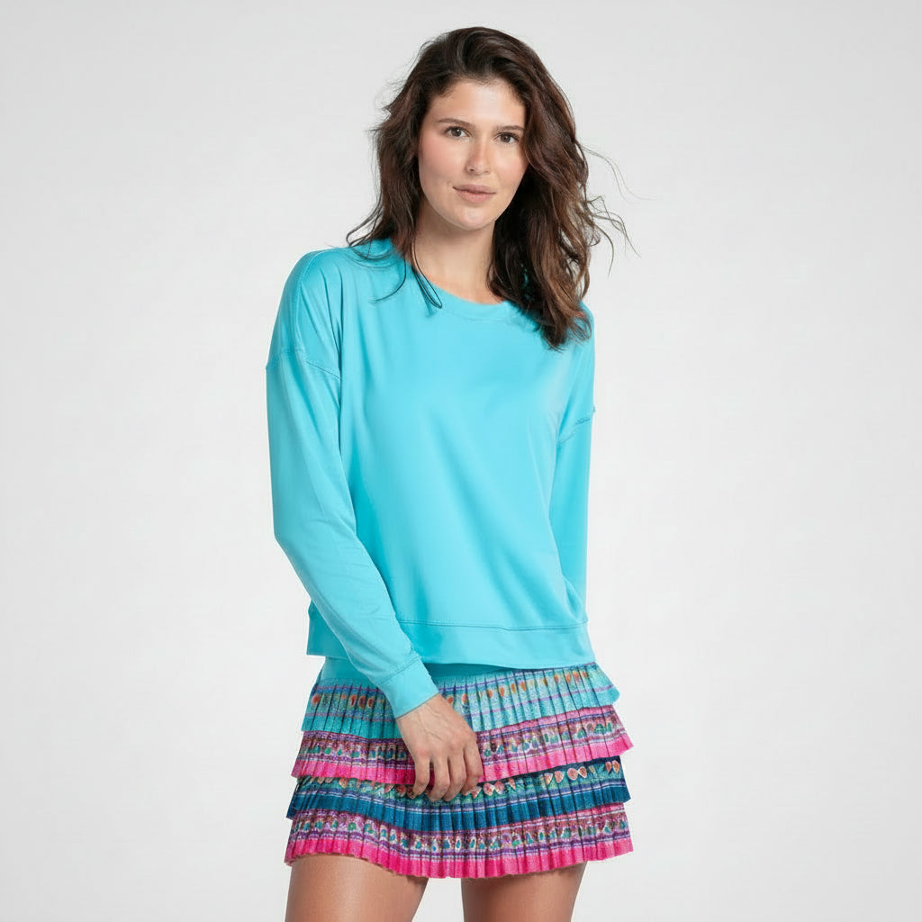 Woman wearing a light blue long-sleeve top and colorful floral print pleated tennis skirt with a on a white background 