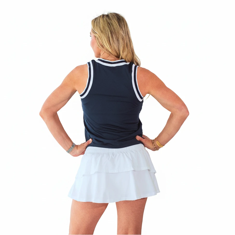 Woman wearing a navy sleeveless top and white tennis skirt against a light blue wall.