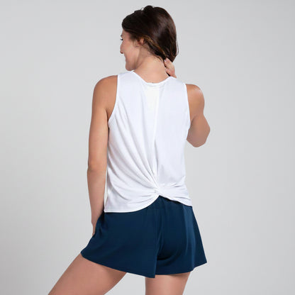 Back view of a woman wearing a hip length white sleeveless tank top that twists in the back and navy shorts on a white background