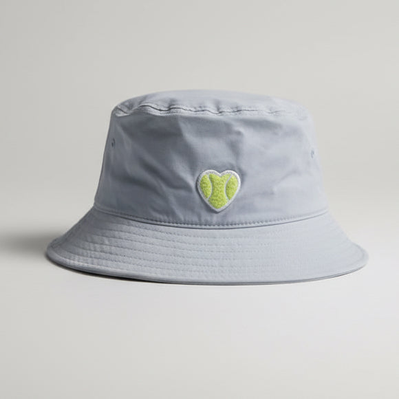 Light powder blue bucket hat with a heart shaped chenille tennis patch sitting on a yellow bench.
