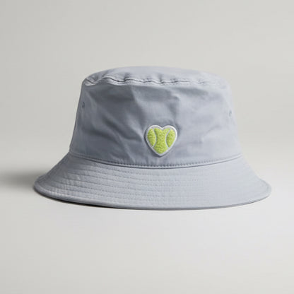 Light powder blue bucket hat with a heart shaped chenille tennis patch sitting on a yellow bench.