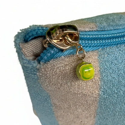 Close-up of a striped pouch with a gold clasp and green tennis ball zipper charm on a white background