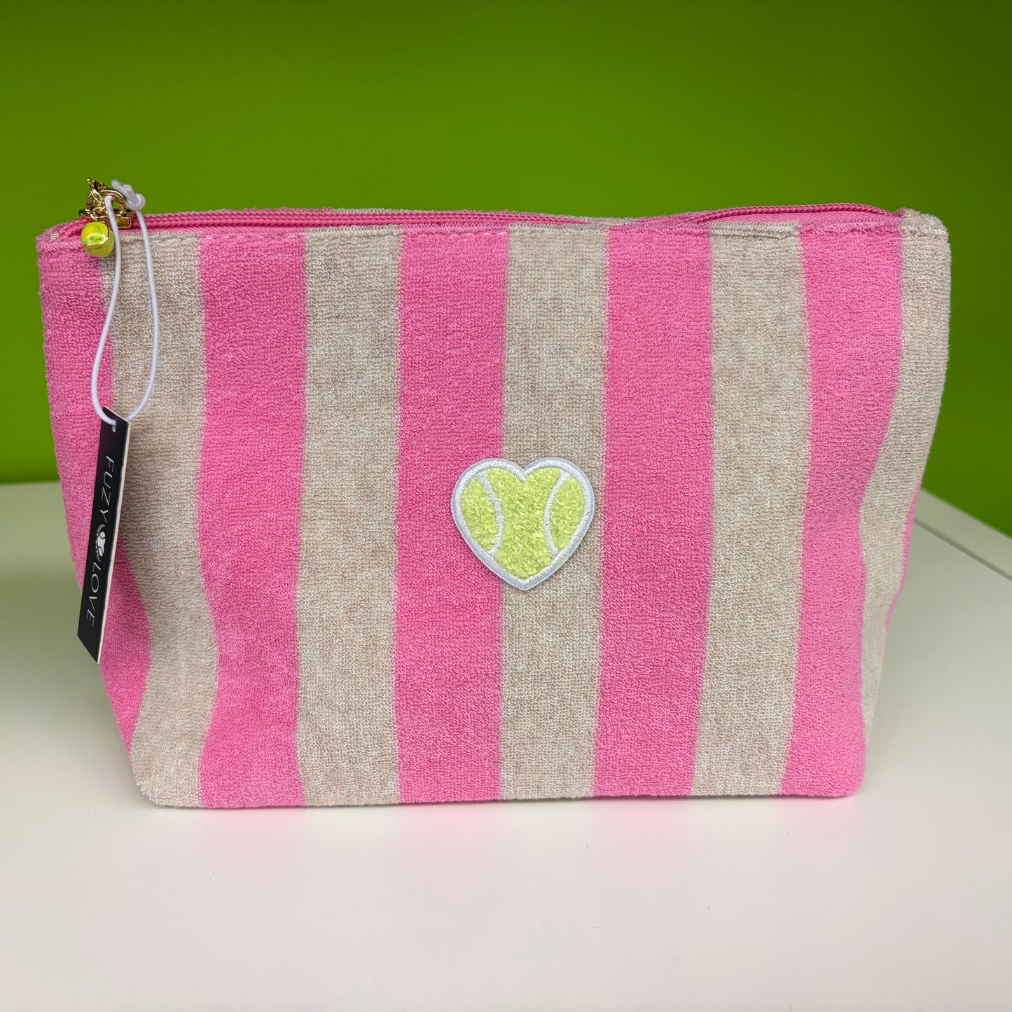 Pink and beige striped pouch with a heart-shaped tag on a white surface with a green background