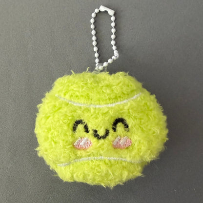 Yellow fuzzy keychain shaped like a tennis ball with decorative elements on a gray background