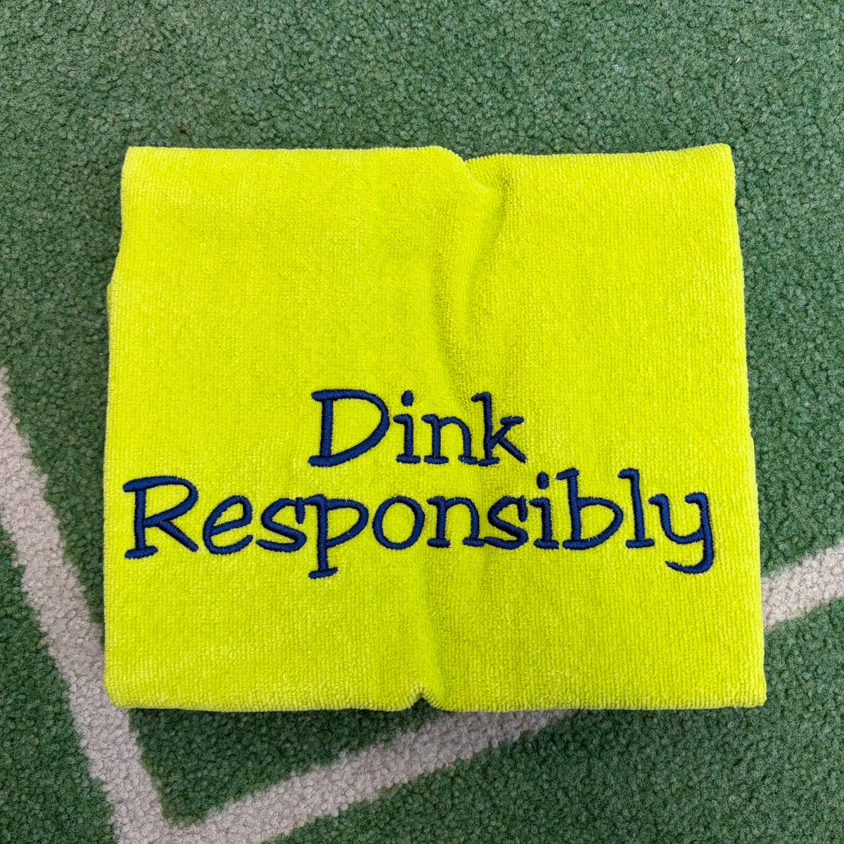 Neon green towel embroidered with the navy Dink Responsibly phrase