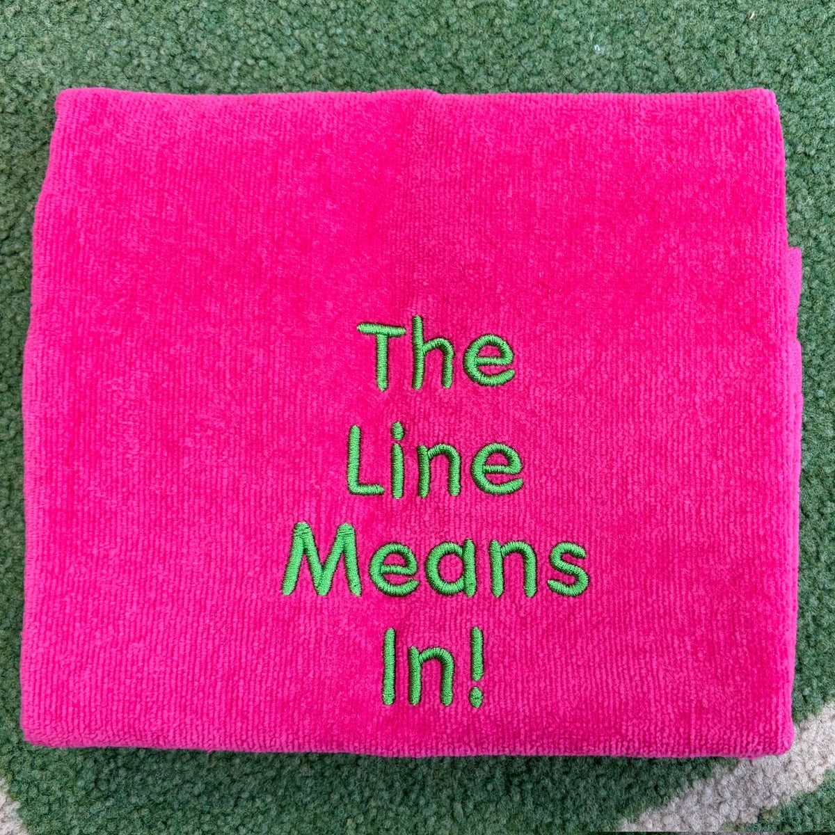 Hot pink towel embroidered with green The Line Means In lettering