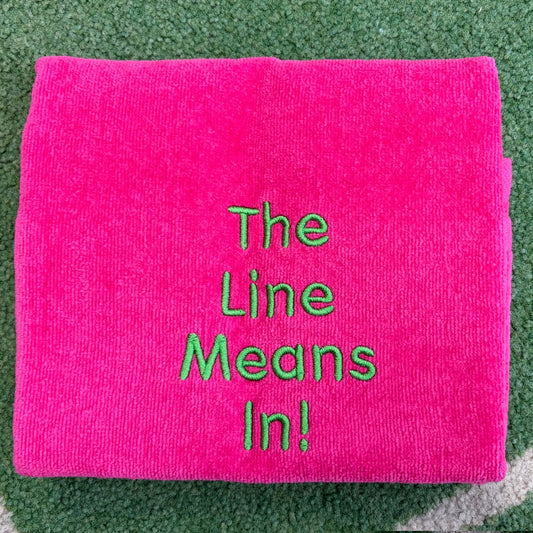 Hot pink towel embroidered with green The Line Means In lettering