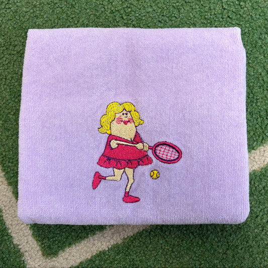 Lavender towel embroidered with a tennis-playing character holding a racket and ball
