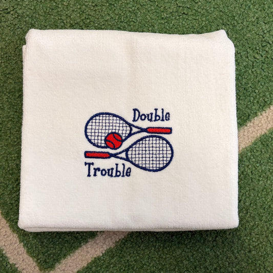 White towel embroidered with Double Trouble, tennis rackets, and a red ball