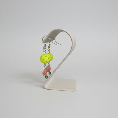 Side view of yellow mini picklball drop earring with pink flower bead and green crystal on a white surface.