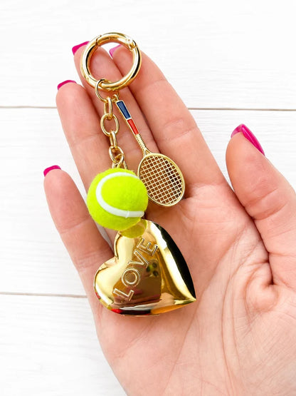 Fuzy Love gold-tone LOVE keychain with tennis ball and red-blue racket charms in hand