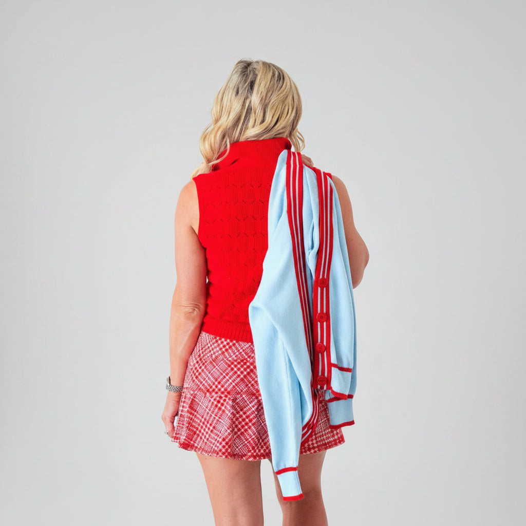 Back view of woman wearing red polo sweater and red hounds tooth print tennis skirt.