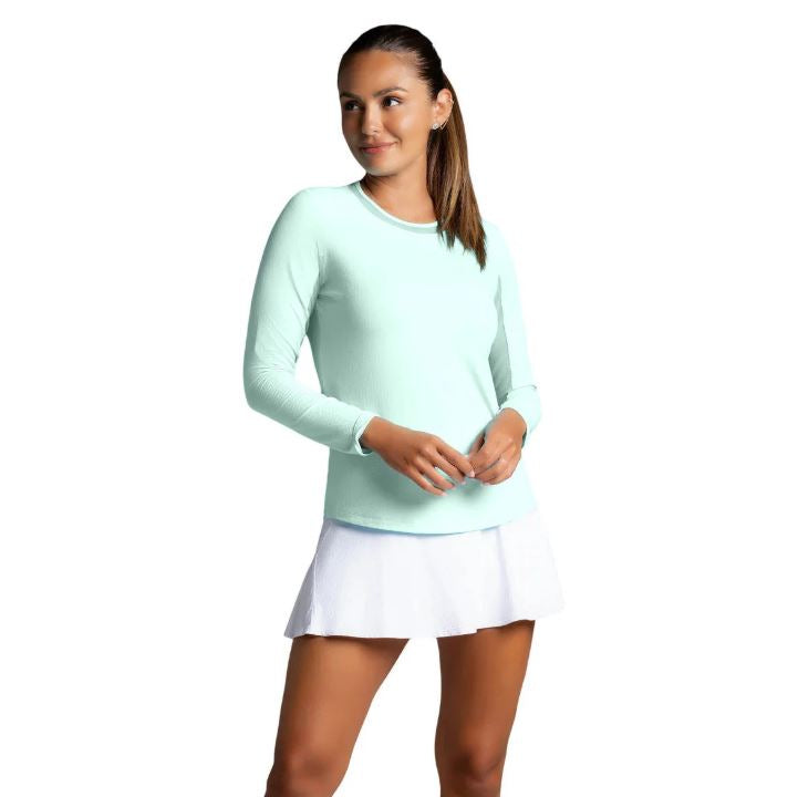 Woman wearing a light blue long-sleeve top and white tennis skirt on a white background