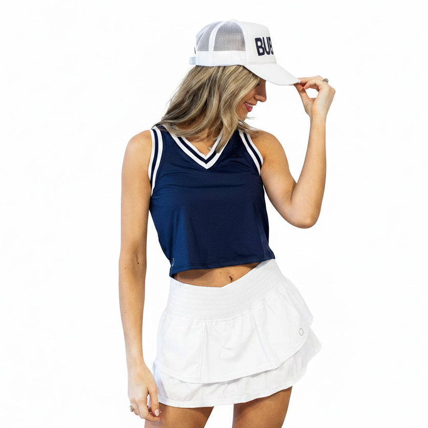 A close-up of a woman in a navy crop top and white tennis skirt with a ruffled design and a built-in pocket, featuring a wider waistband and silicone grips.
