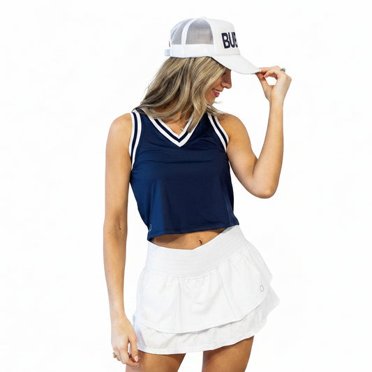 A close-up of a woman in a navy crop top and white tennis skirt with a ruffled design and a built-in pocket, featuring a wider waistband and silicone grips.