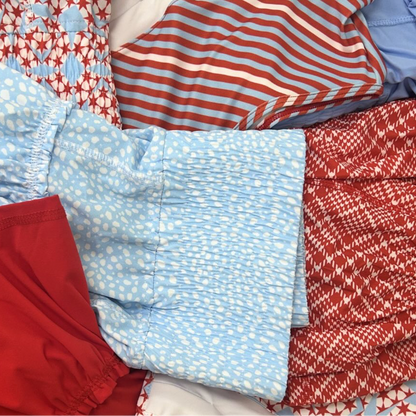 Collection of folded colorful red white and blue tennis skirts with various patterns.