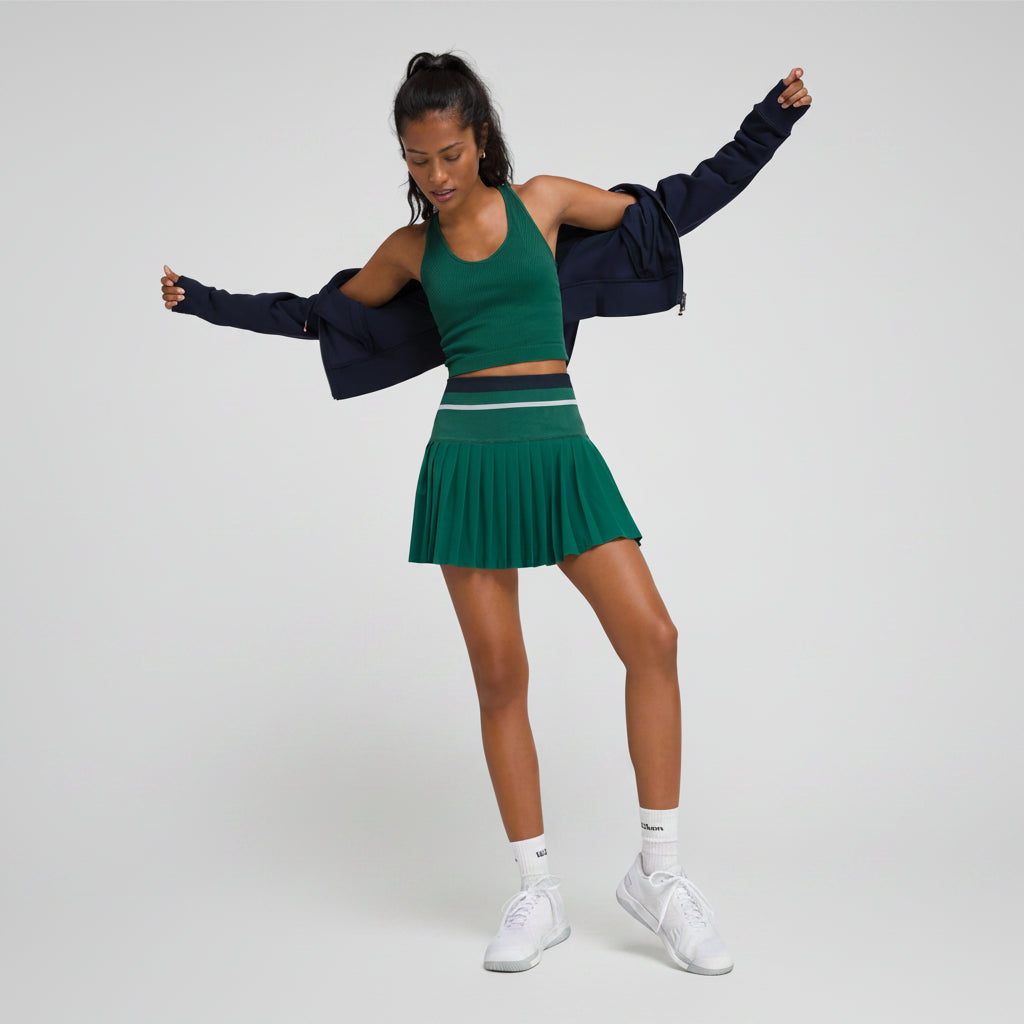 Woman in green athletic tennis outfit with navy jacket on a plain background