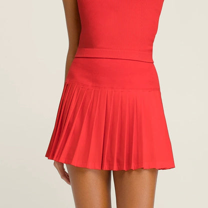 Person wearing a red pleated skirt and white sneakers on a beige background