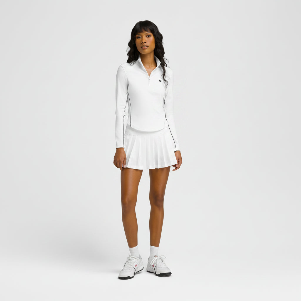 Woman wearing a white tennis outfit with a jacket and skirt on a plain background